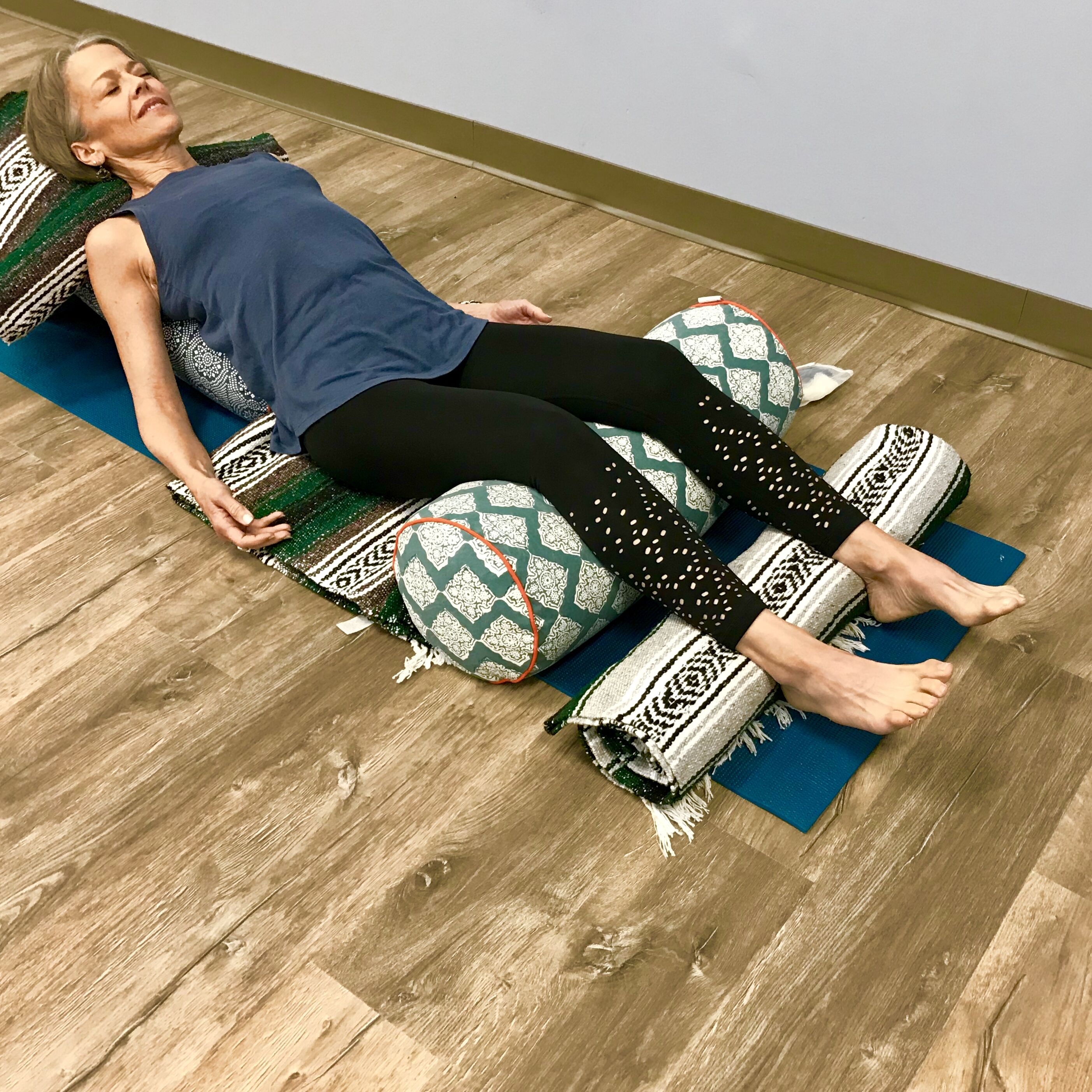 Moya McGinn Mathews demonstrates in a restorative yoga heart opener reclined on a bolster with knees supported on another bolster.